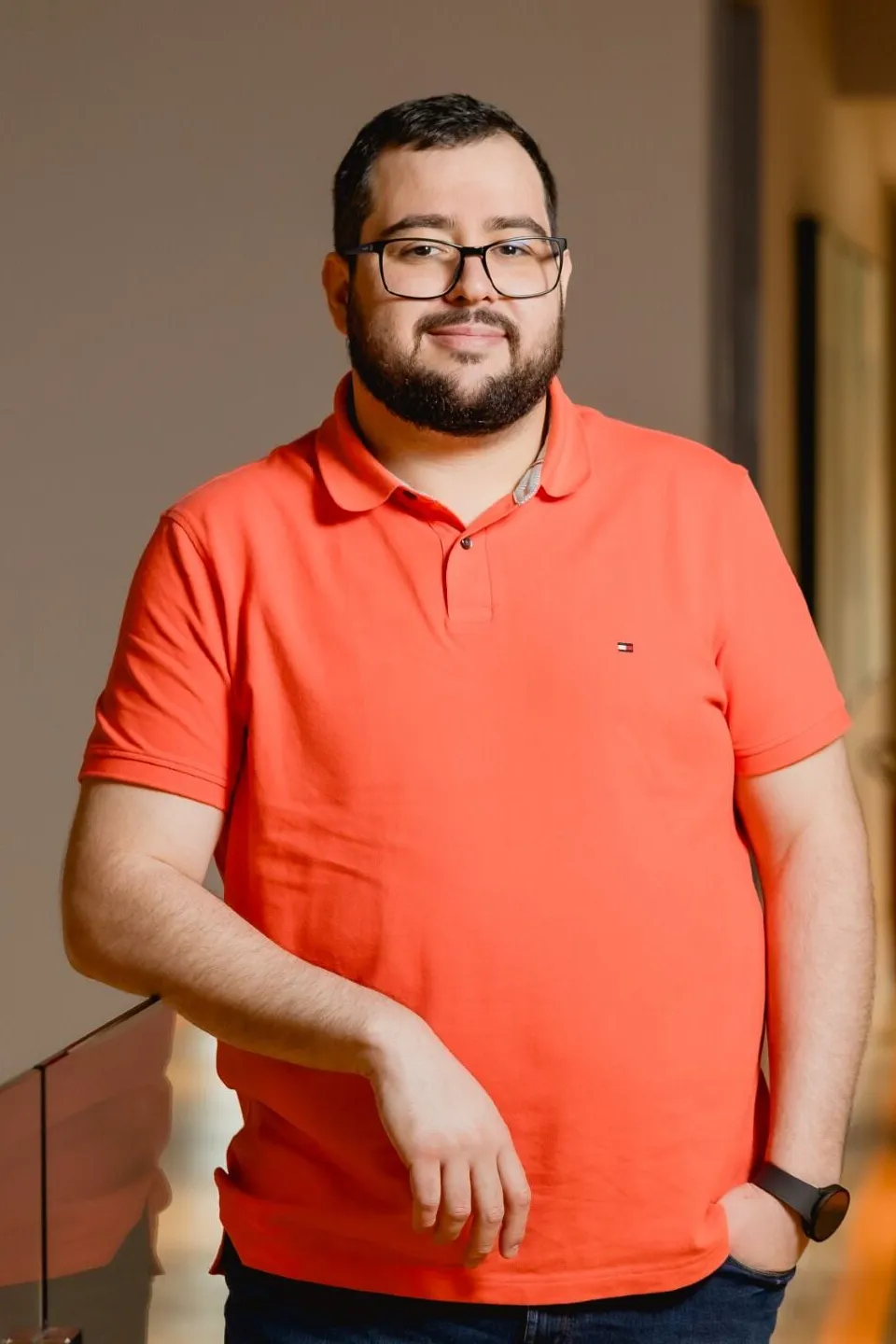 CEO do Efí Bank, Denis Silva, com camisa laranja, óculos e encostado em um muro de vidro