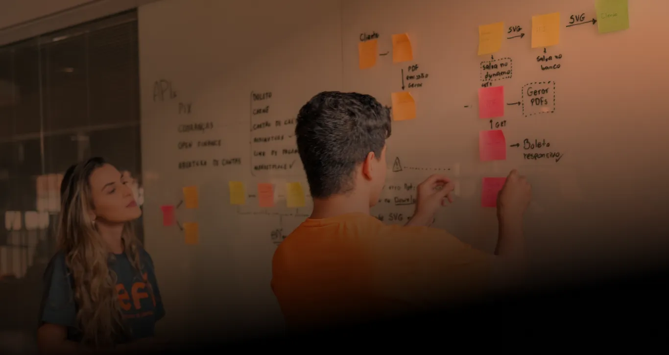 Colaborador do Efí Bank, de costas, vestindo uma camisa laranja e colando adesivos em um quadro de planejamento