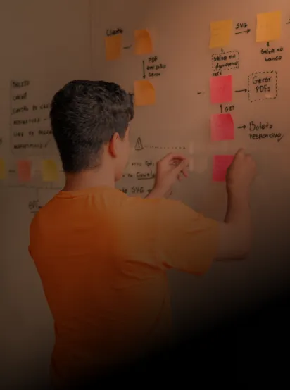 Colaborador do Efí Bank, de costas, vestindo uma camisa laranja e colando adesivos em um quadro de planejamento