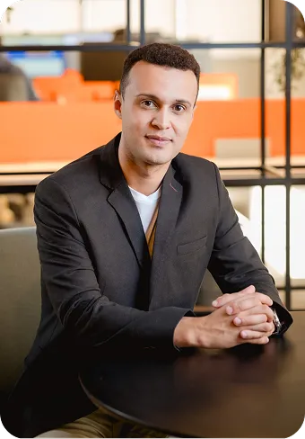 Diretor de conformidade do Efí Bank, Paulo Barros, sentado em uma cadeira, apoiado em uma mesa, de terno preto e camisa branca