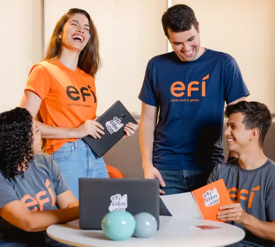 Colaboradores da Efí conversando e sorrindo em uma mesa de reunião
